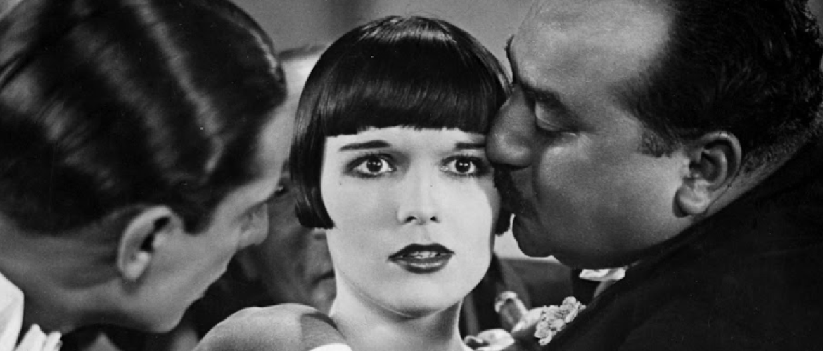 Dos hombre y una mujer de pelo corto. Uno se los hombres le besa en la mejilla