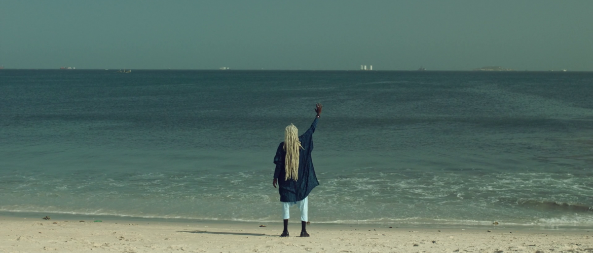 Mujer afro frente al mar alzando la mano