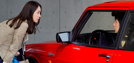 Mujer hablando con un señor que esta en un carro rojo 