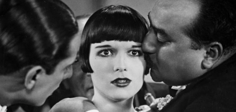 Dos hombre y una mujer de pelo corto. Uno se los hombres le besa en la mejilla